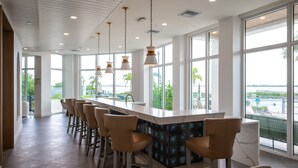 A modern bar area with a long counter, multiple bar stools, and large windows offering a view of a pool and greenery. - Luxury Fragrance-Free Bayfront Retreat with Saltwater Pool (Clearwater)