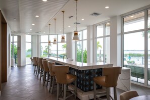 A modern bar area with a long counter, multiple bar stools, and large windows offering a view of a pool and greenery.