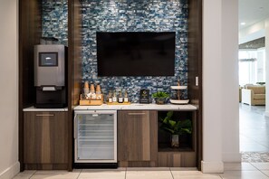 A modern kitchen with a built-in refrigerator, a coffee machine, and a flat-screen TV mounted above a backsplash with a blue and white pattern.
