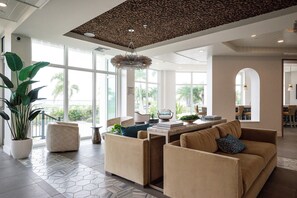 A spacious lobby with a high ceiling, large windows, and a central seating area with sofas and a coffee table.