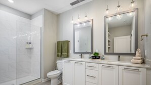 A modern bathroom with a glass shower enclosure, a toilet, and a vanity with a large mirror. - Luxury Fragrance-Free Bayfront Retreat with Saltwater Pool (Clearwater)
