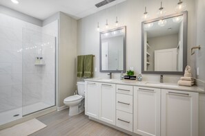A modern bathroom with a glass shower enclosure, a toilet, and a vanity with a large mirror.