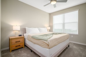 A bedroom with a bed, bedside lamps, a nightstand, a ceiling fan, and a window with blinds.