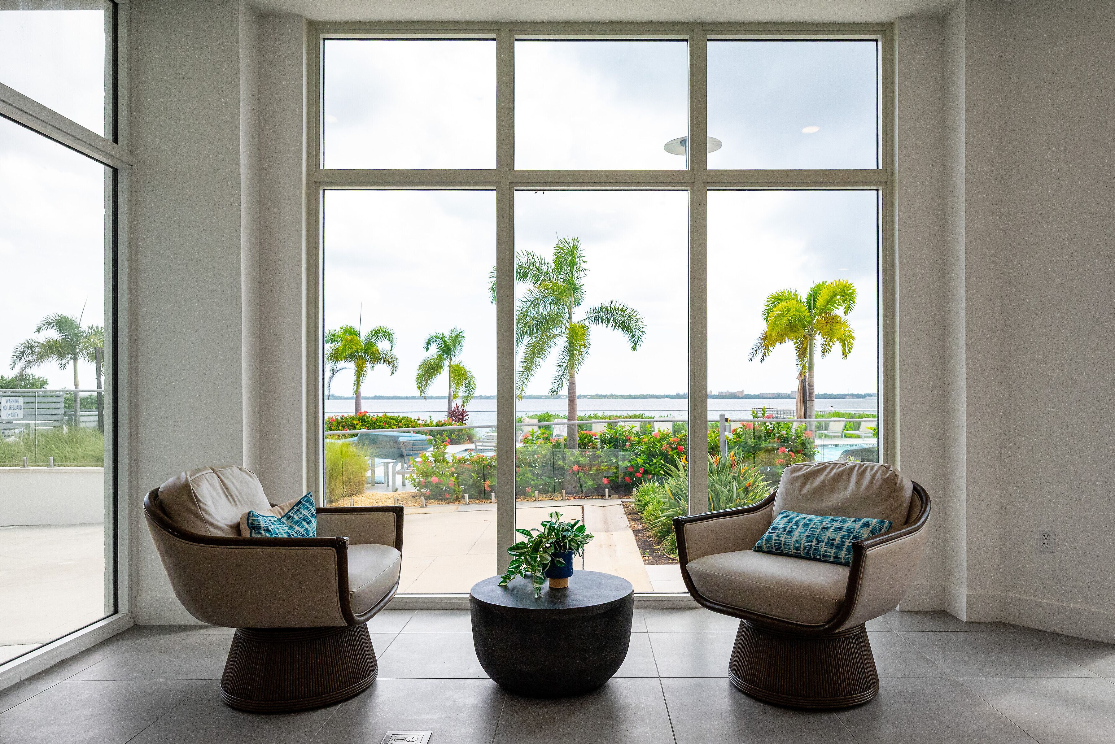 A spacious room with large windows, two armchairs, a coffee table, and a view of a landscaped outdoor area.