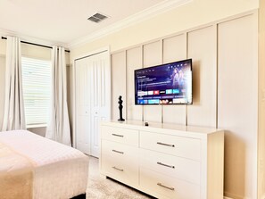 A bedroom with a bed, a TV mounted on the wall, a dresser, and a window with curtains. - Family Fun: Private Pool, Themed Rooms & Summer Kitchen - Walk to Clubhouse (Kissimmee)
