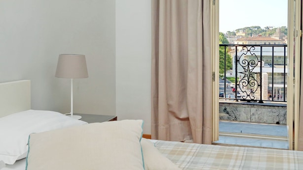 A bedroom with a bed, a nightstand, a lamp, and a view of a balcony with a railing.
