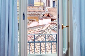 Une vue à travers une porte ouverte, surmontée d’un portail en métal, qui donne sur un balcon doté d’un toit en tuiles.