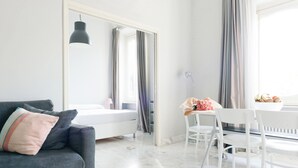 A modern bedroom with a bed, a grey sofa, a white chair, and a mirror.