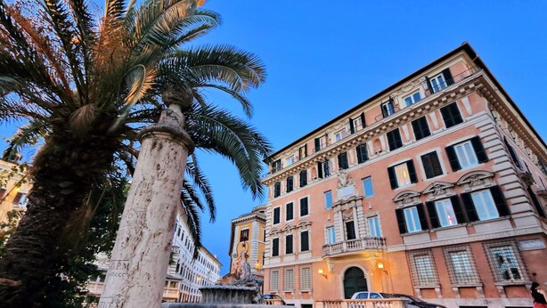 A historic building with classical architecture, a fountain in the foreground, and a palm tree. - Fontana Più Stella (Rome)