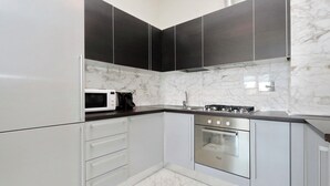 A modern kitchen with white cabinets, a stainless steel oven, and a microwave.