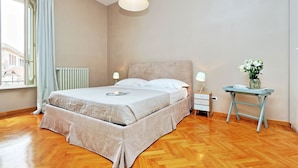 A hotel room with a bed, bedside tables, a radiator, a window with curtains, and a view of buildings outside. - Fontana Più Stella (Rome)