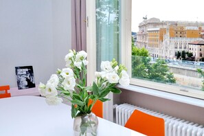 A room with a table, a vase with white flowers, a radiator, and a window with a view of a historic building. - Fontana Più Stella (Rome)