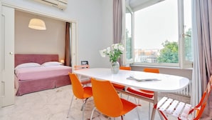 A hotel room with a bed, a dining table with chairs, a vase with flowers, and a window with curtains. - Fontana Più Stella (Rome)