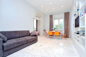 Un salon moderne avec un canapé gris, une table à manger avec des chaises orange et une bibliothèque blanche.