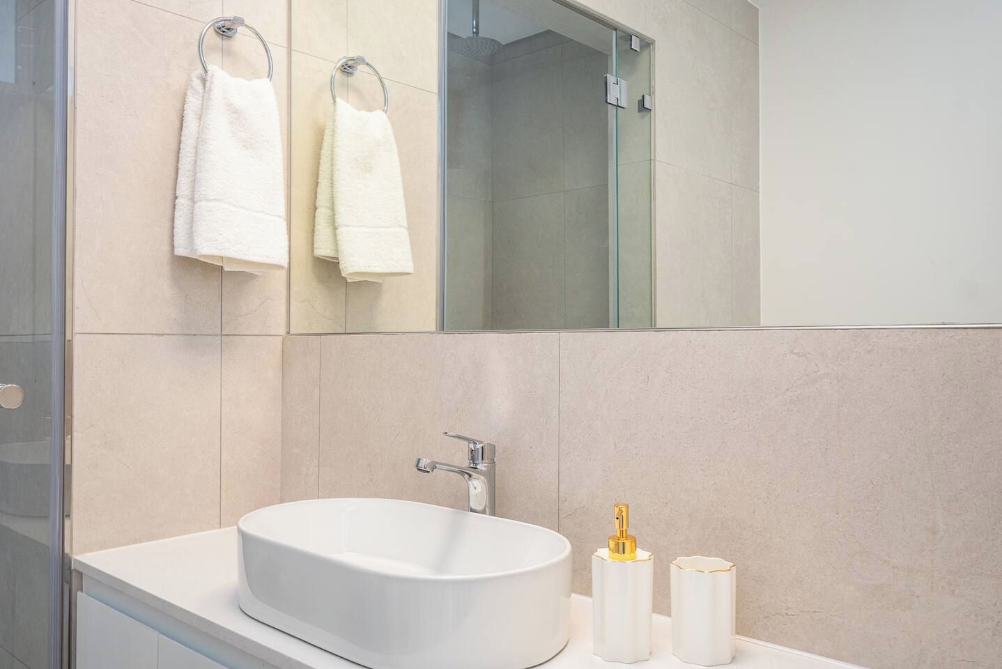 Un baño moderno con un lavamanos grande, dos toallas colgadas en un perchero y una cabina de ducha de vidrio.