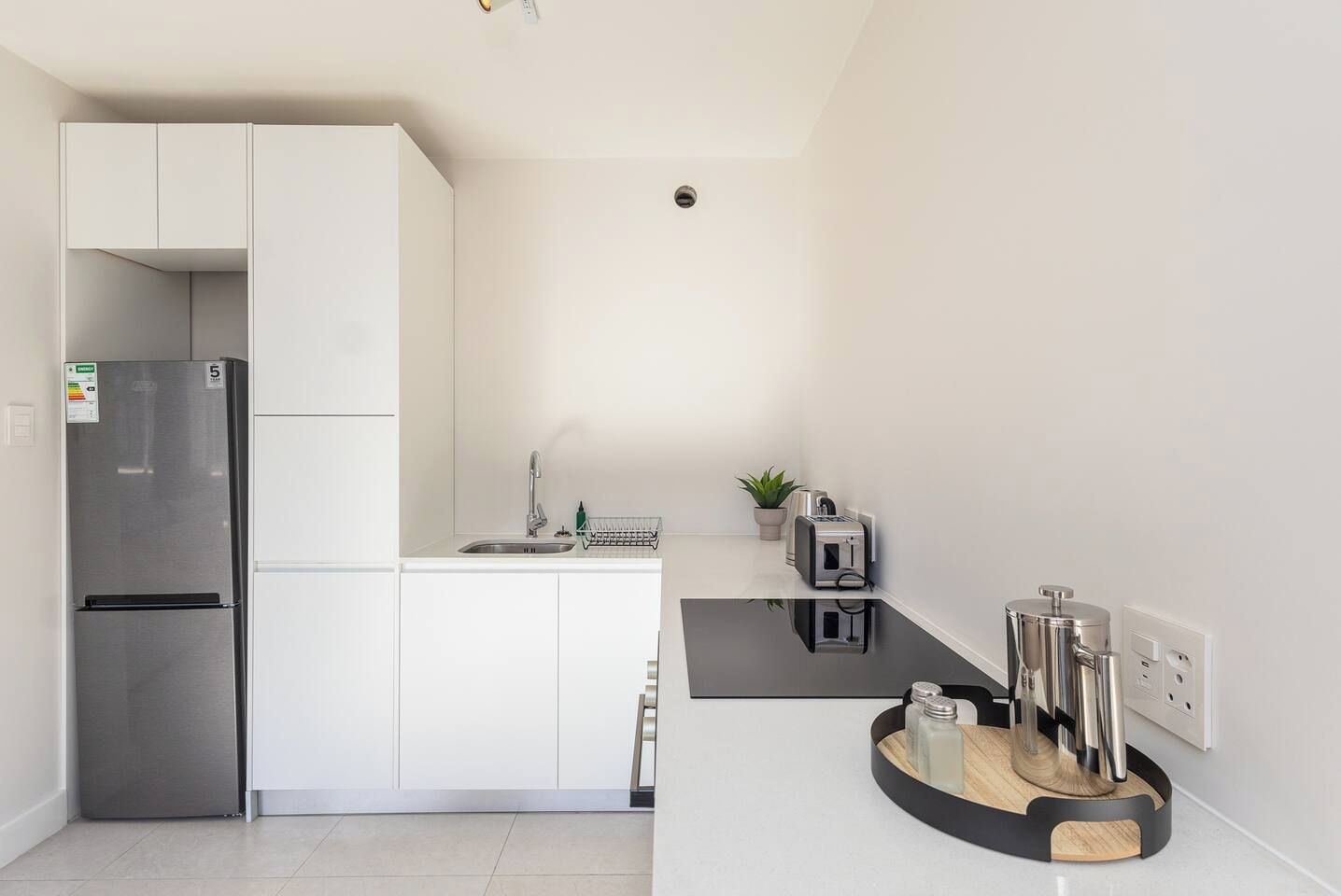 A modern kitchen with white cabinetry, a stainless steel refrigerator, a sink, and a countertop with a toaster and a coffee machine.