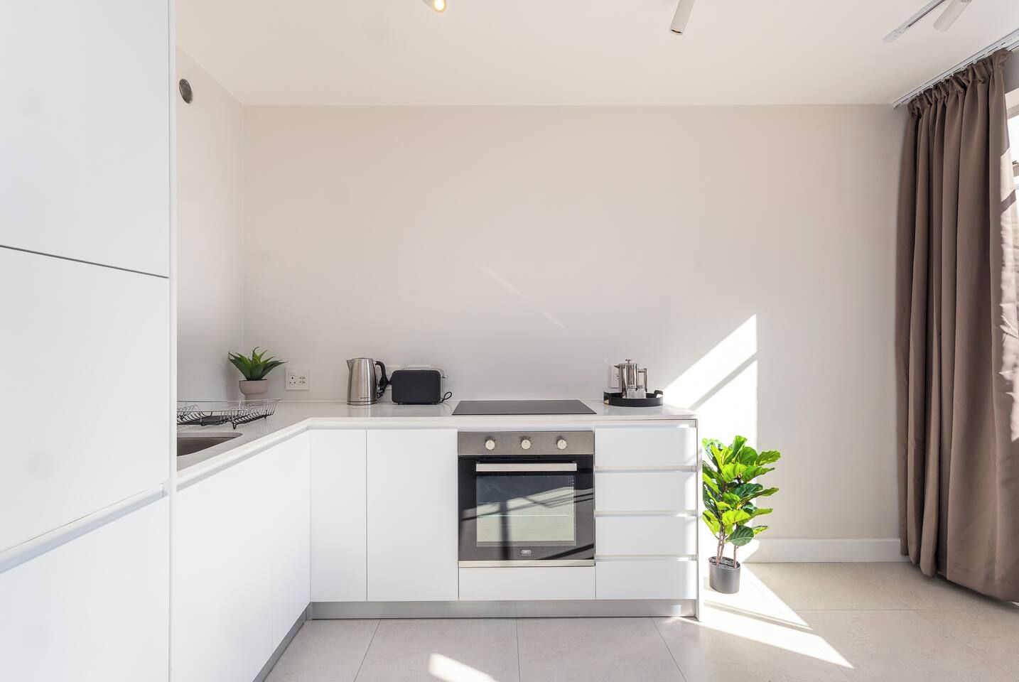 Una cocina moderna con armarios blancos, horno empotrado y cafetera.