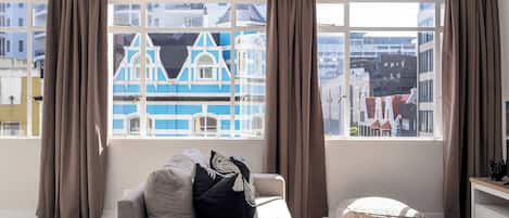 A modern living room with a sofa, a coffee table, and a view of a blue building through large windows.