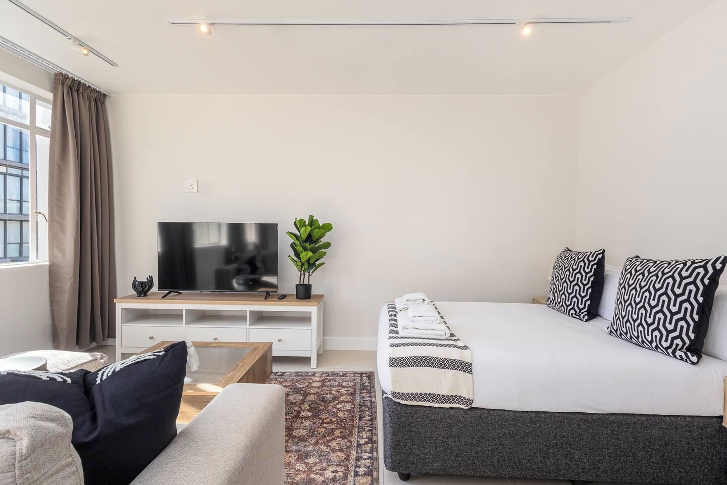 Ein modernes Hotelzimmer mit Bett, Fernseher, kleinem Schreibtisch und einem Fenster mit Vorhängen.