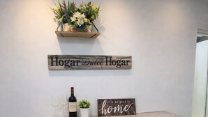 A small dining area with a wooden table, two wine glasses, a bottle, and a chair. Above the table, there are two signs: one reads 'Hogar Dulce Hogar' and the other says 'it's so good to home.' - Exclusiveapt Wifi Balcony Tv Laundry Medellín (Medellín)