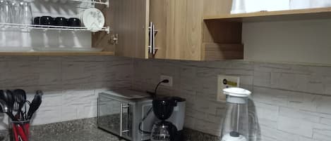 Una cocina con armarios de madera, microondas, licuadora, tostadora y un escurreplatos con platos y vasos.