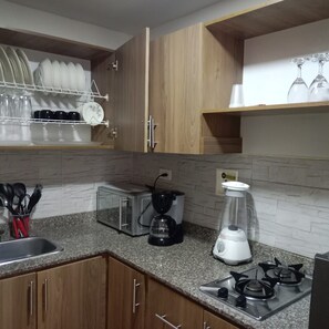 Eine Küche mit Holzschränken, einer Mikrowelle, einem Mixer, einem Toaster und einem Geschirrgestell mit Tellern und Gläsern.