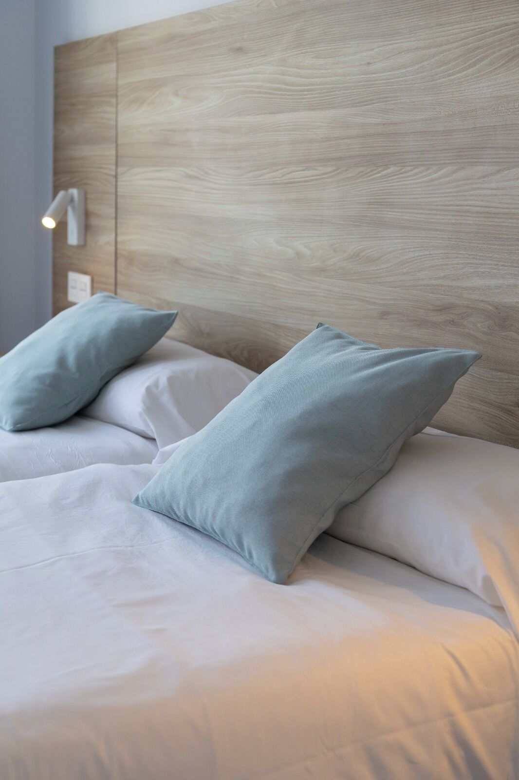 Ein Bett mit hölzernem Kopfteil, zwei Kissen und einer Nachttischlampe.