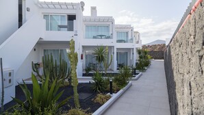 A modern residential building with a covered outdoor area, a paved walkway, and various desert plants. - Quiet Studio with Sea View & Pool in Puerto del Carmen (Puerto del Carmen)