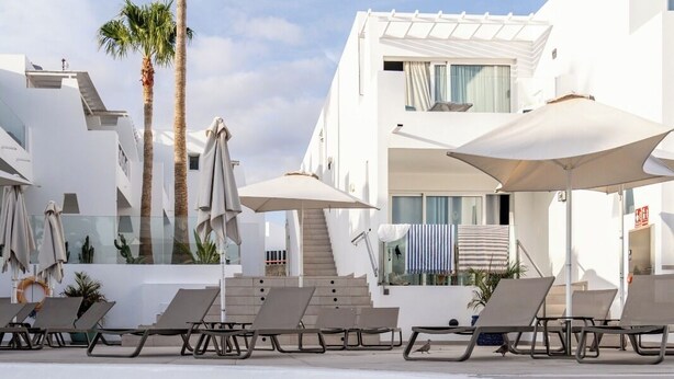 A pool area with lounge chairs and umbrellas, a staircase leading to an upper level, and palm trees. - Quiet Studio with Sea View & Pool in Puerto del Carmen (Puerto del Carmen)