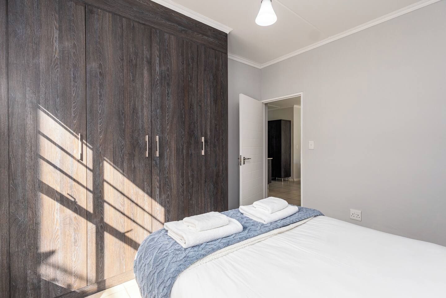Ein Schlafzimmer mit großem Kleiderschrank, einem Bett mit weißer Bettwäsche und Blick auf ein Treppenhaus.