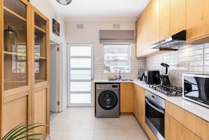 A compact kitchen with wooden cabinets, a washing machine, a stove, and a microwave. - Pet-friendly Studio with Private Patio by Ctha (Cape Town)