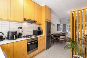 A modern kitchen with wooden cabinets, a gas stove, a built-in oven, a microwave, and a refrigerator. - Pet-friendly Studio with Private Patio by Ctha (Cape Town)