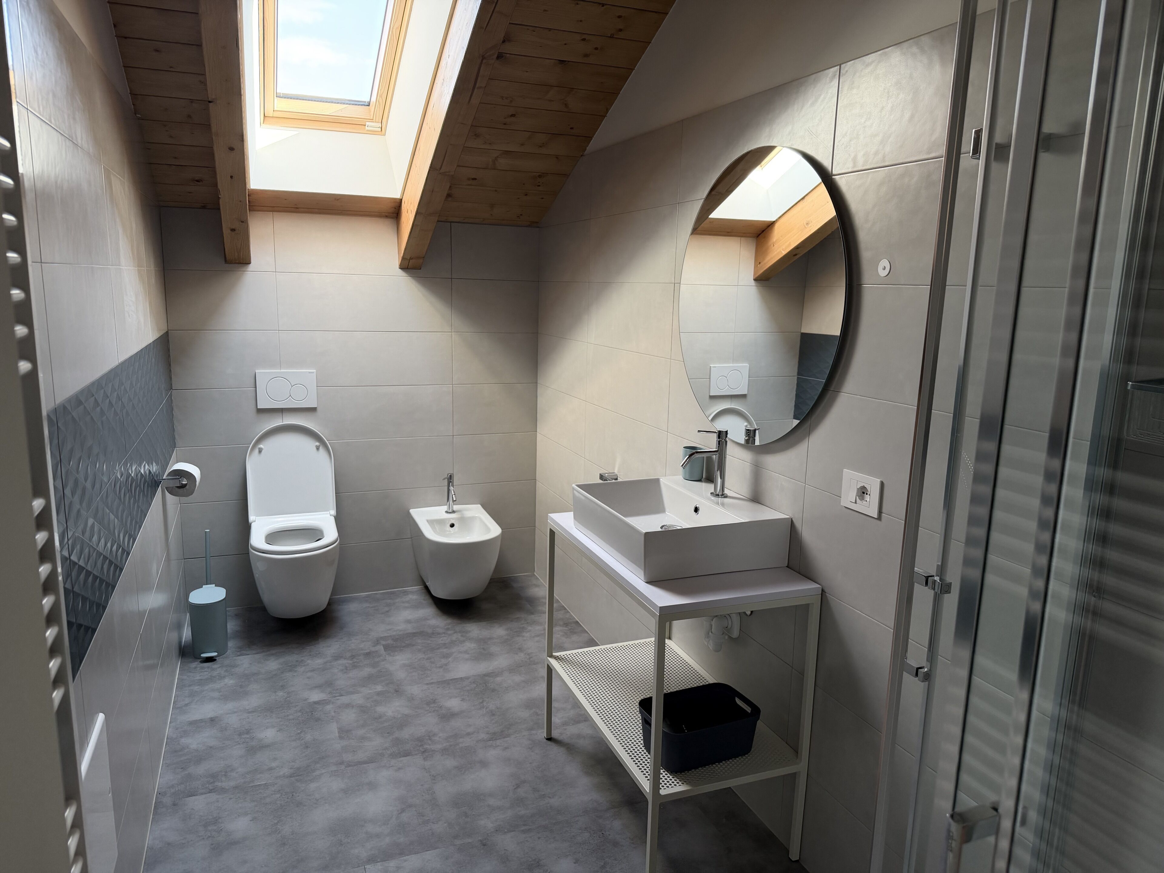 Ein modernes Badezimmer mit Oberlicht, einem Bidet, einer Toilette, einem Waschbecken und einem Spiegel.
