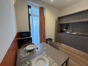 A compact kitchen with modern appliances, a dining area with a table set for two, and a window with curtains. - Mirage Arona (Arona)