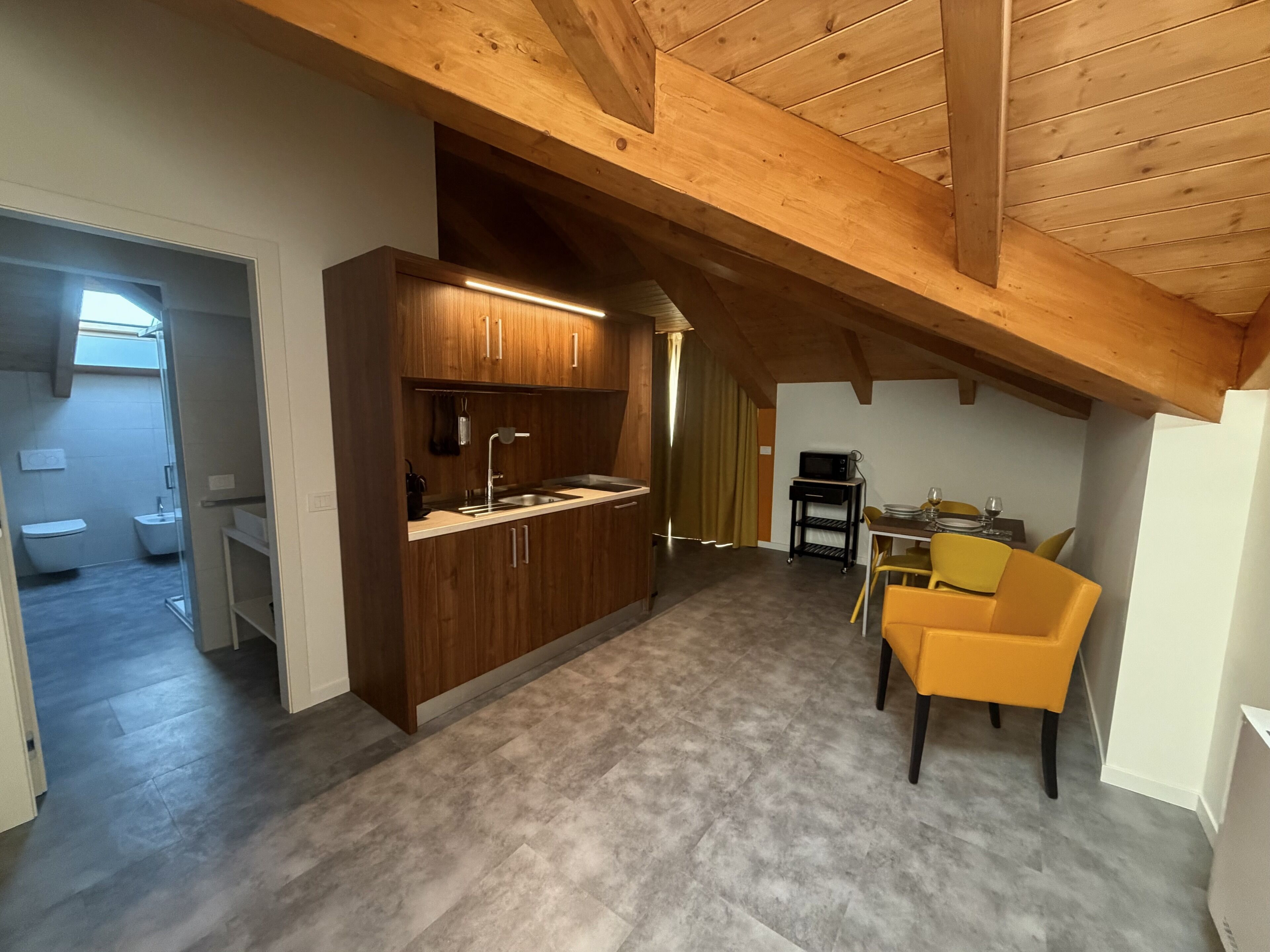 A compact kitchen with wooden cabinets, a built-in microwave, and a dining area with yellow chairs.