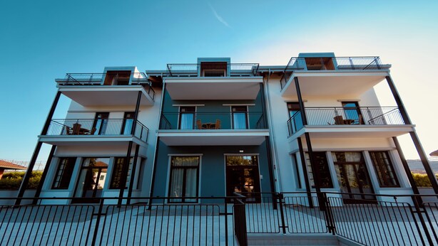 A multi-story residential building with balconies, a central entrance, and a staircase leading to the entrance.