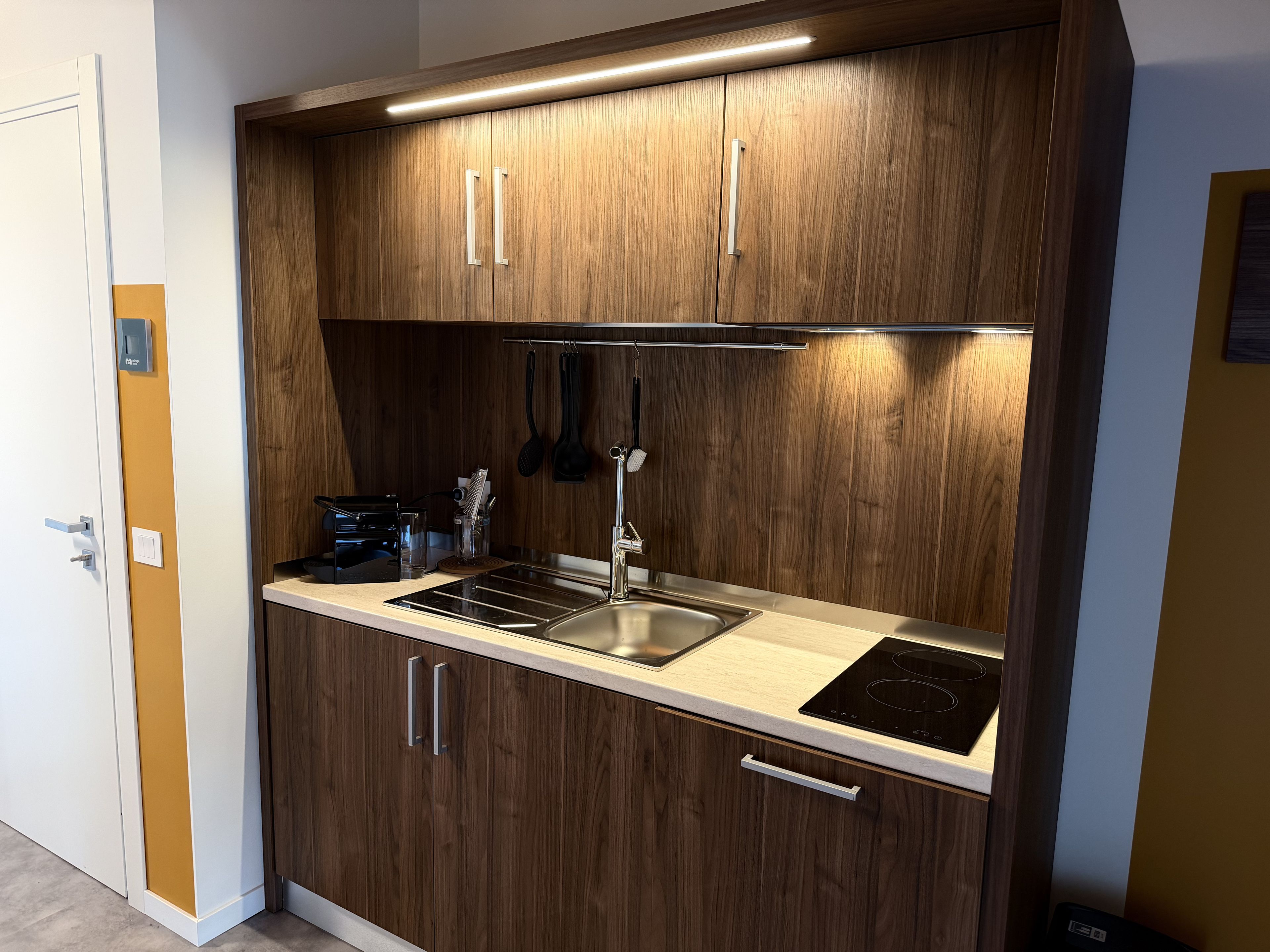 A compact kitchen with wooden cabinets, a stainless steel sink, and an induction cooktop.