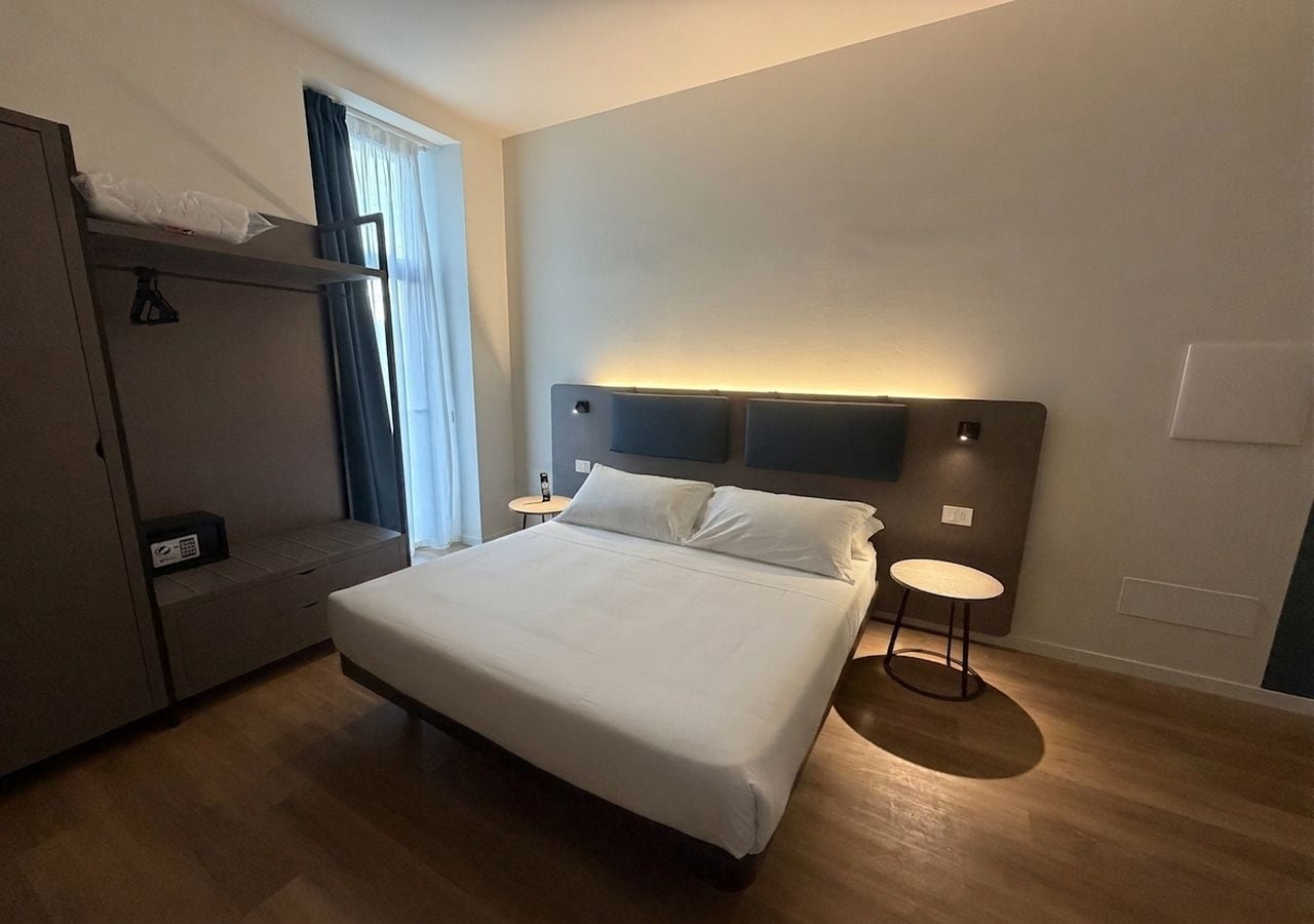 A hotel room with a bed, bedside table, and a wardrobe.