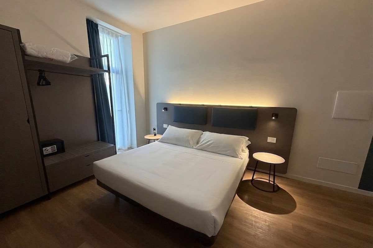 A hotel room with a bed, bedside table, and a wardrobe.