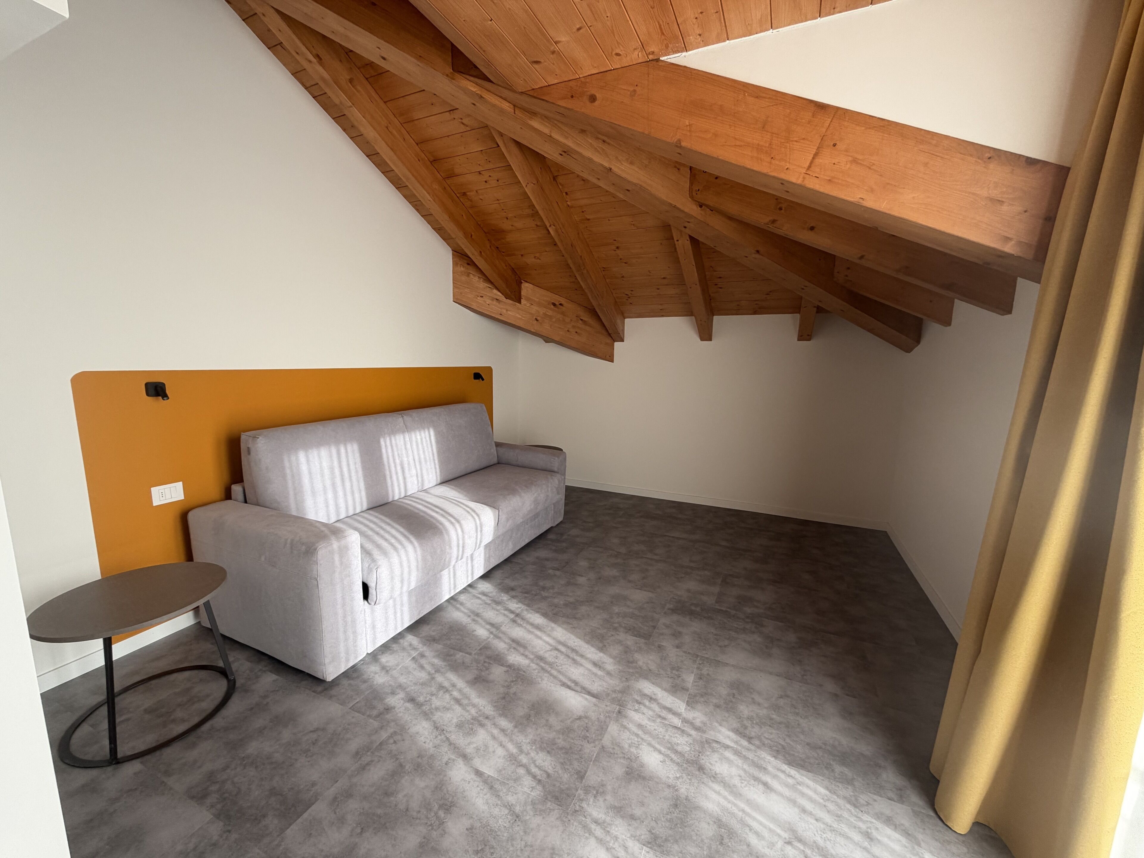 Una habitación pequeña y moderna con un sofá gris, una mesita redonda y una estructura de techo de madera.