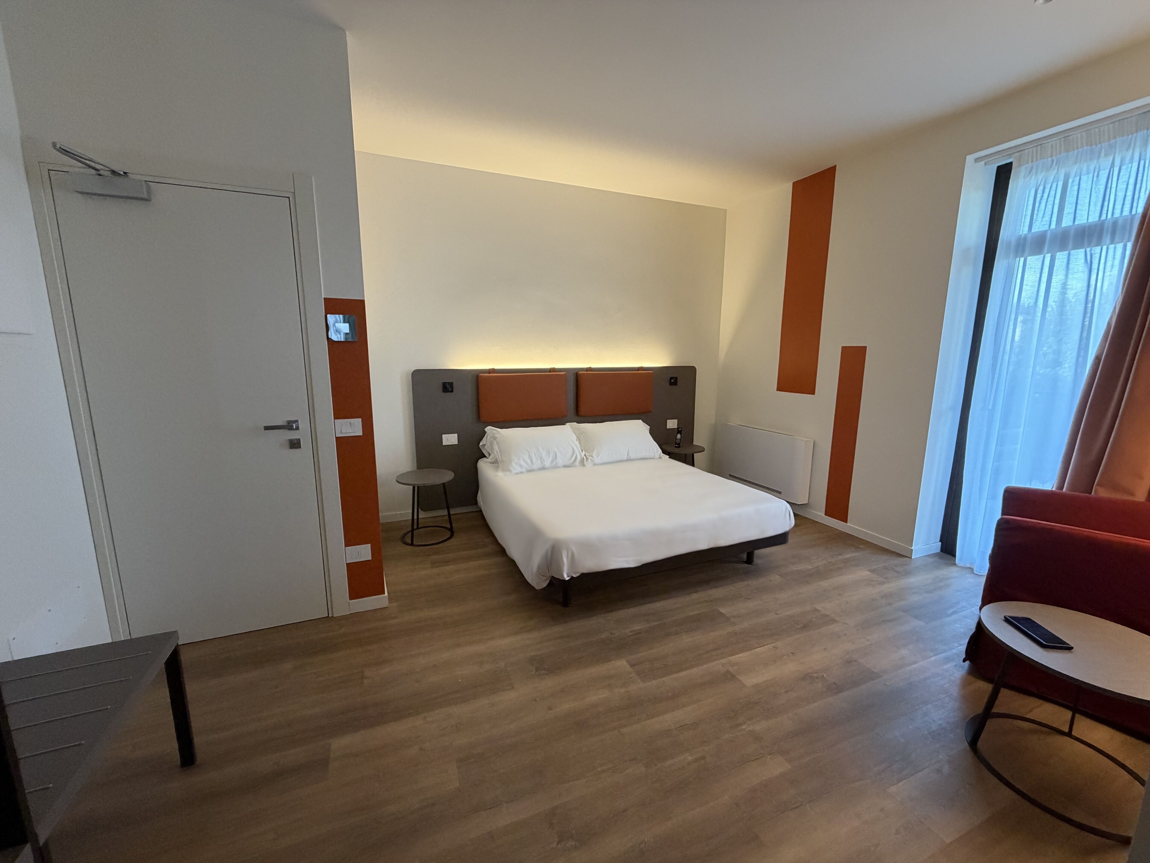 A hotel room with a bed, bedside tables, a chair, and a view of the outdoors.