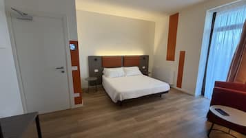 A hotel room with a bed, bedside tables, a chair, and a view of the outdoors.