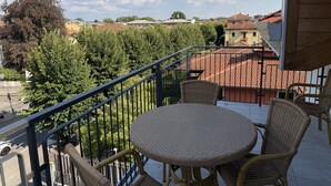 A balcony with wicker furniture, a view of a residential area, and a clear sky.