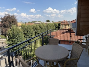 A balcony with wicker furniture, a view of a residential area, and a clear sky.