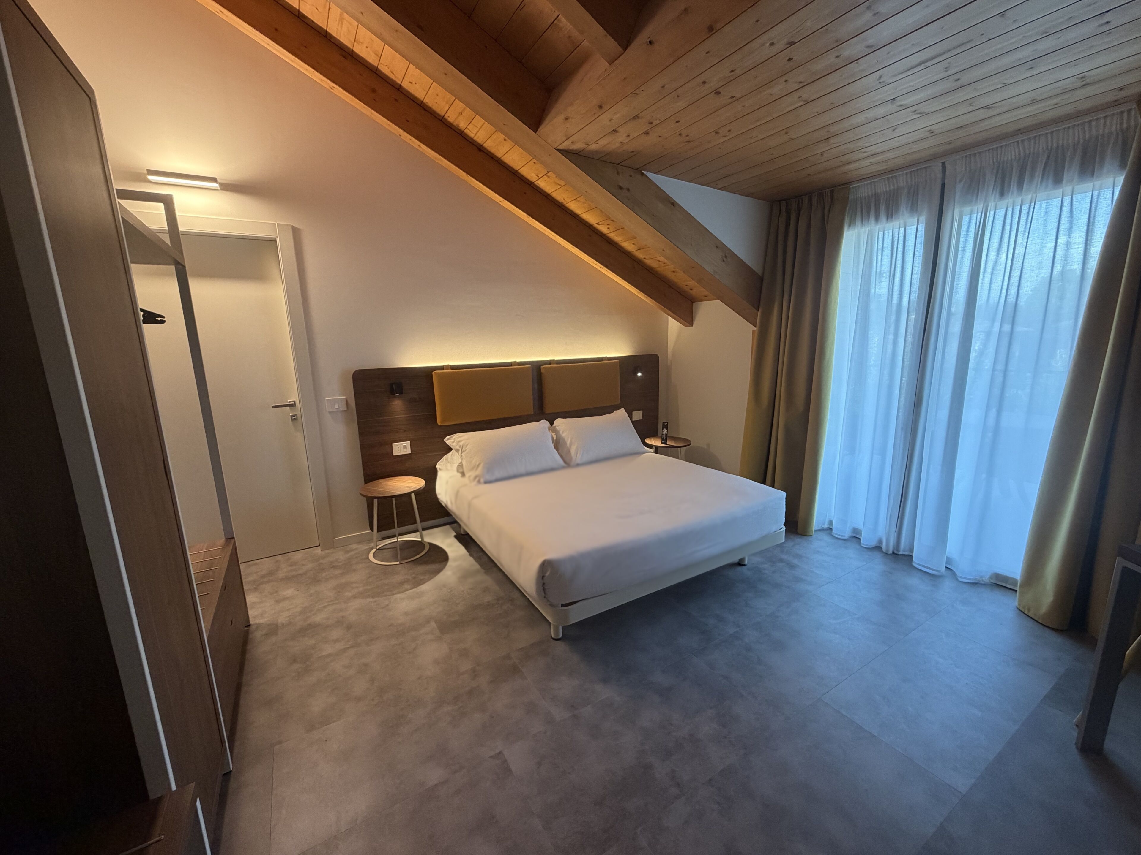 Een hotelkamer met een groot bed, een houten plafond, een klein nachtkastje en een deur.