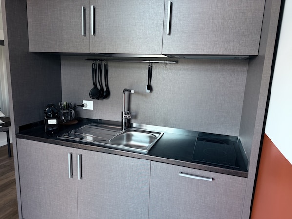 A modern kitchen with a stainless steel sink, black countertop, and grey cabinets.