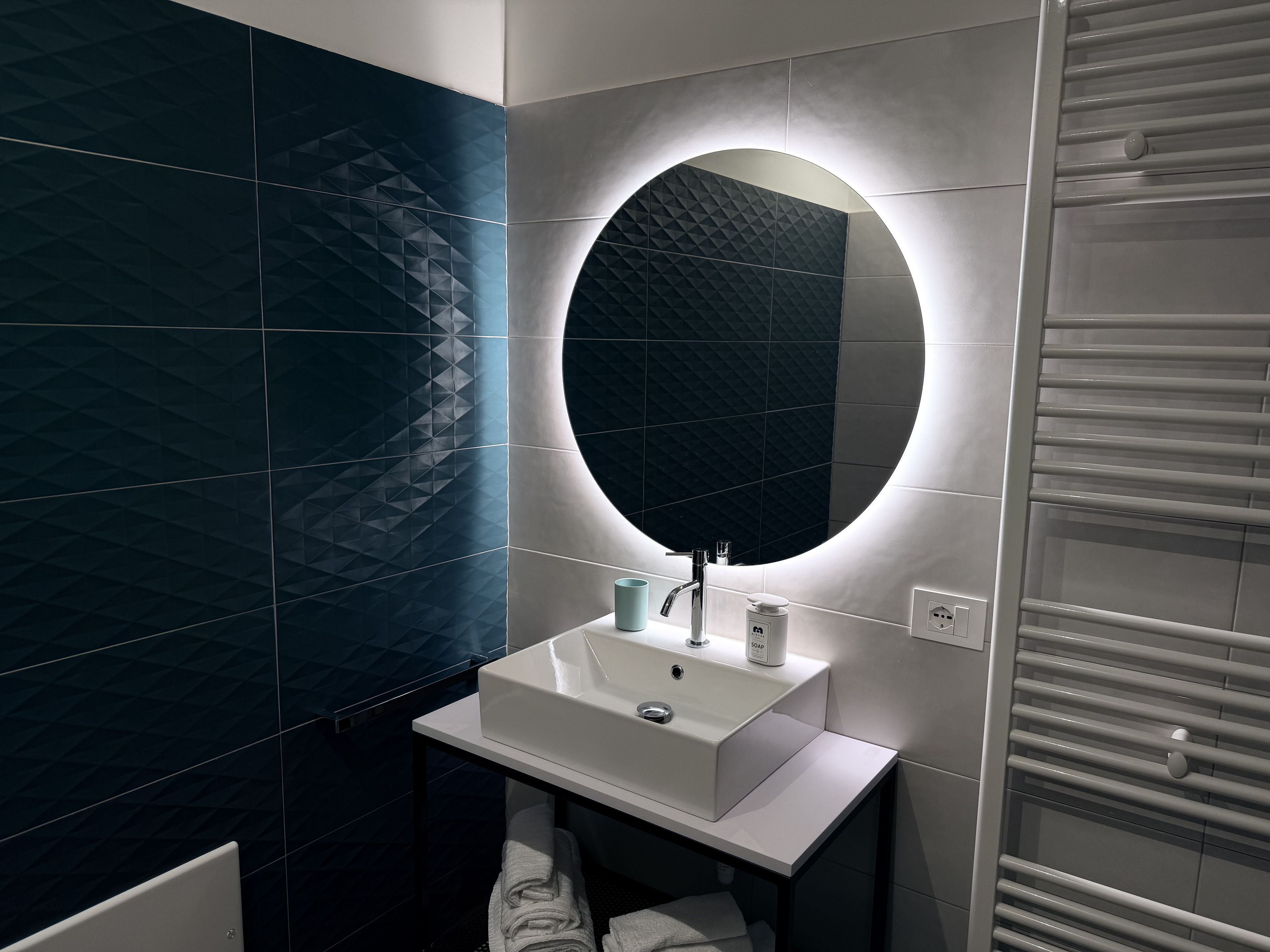 A modern bathroom with a white sink, a round mirror, and a towel rack.