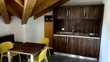A compact kitchen with dark wooden cabinets, a stainless steel sink, and a dining area with a wooden table and yellow chairs.