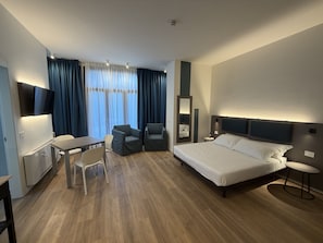 Ein modernes Hotelzimmer mit Bett, Schreibtisch, Sesseln und Fernseher.