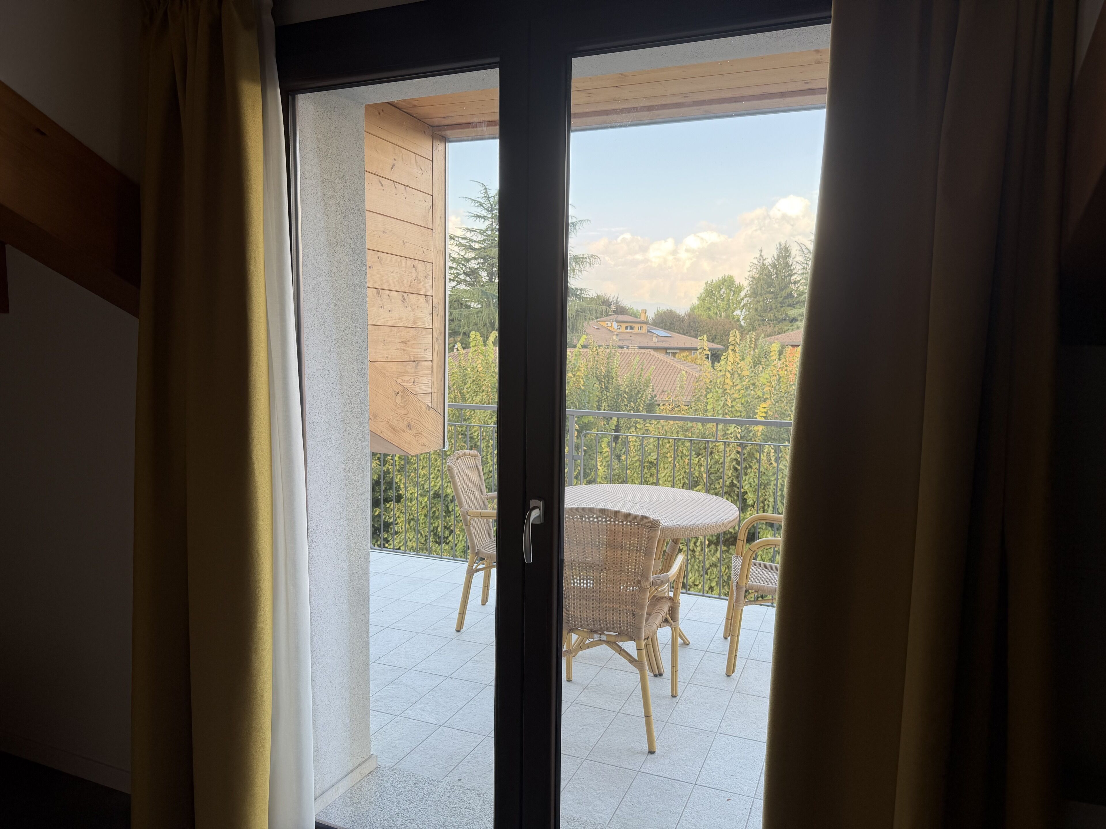 A view through a sliding glass door to an outdoor balcony with wicker furniture and a tiled floor.
